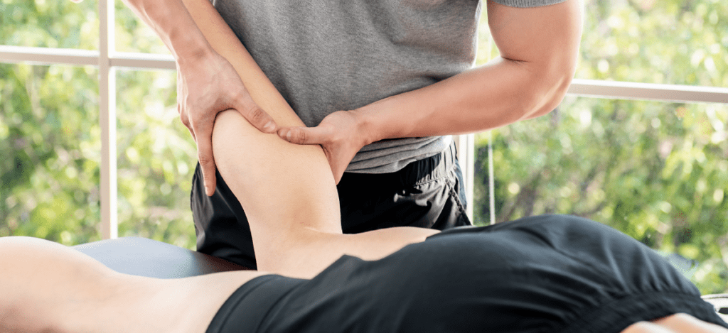 Massage therapist conducting deep-tissue massage therapy on an athlete's calf. Patient is lying on his front with his left leg bent upwards at the knee.
